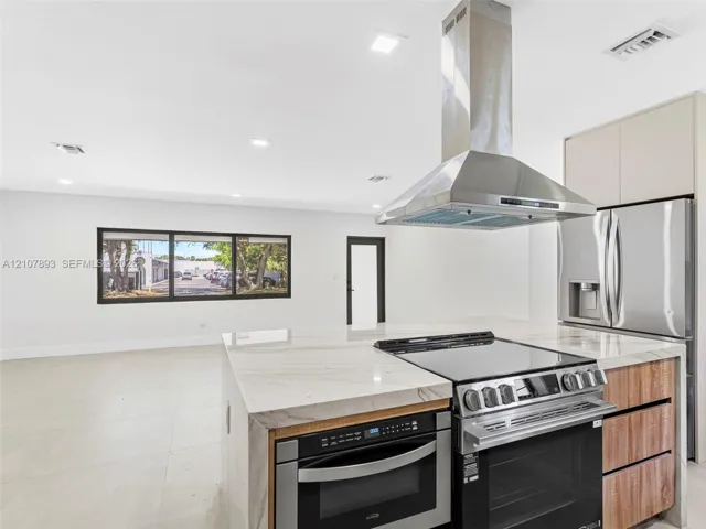 Kitchen featuring an island with a waterfall-edge countertop, stainless steel range hood, integrated built-in oven, and wood-finish cabinetry