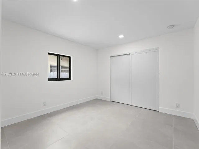 Neutral-toned large-format tile flooring, recessed ceiling lighting, sliding-panel closet doors, and a window with a black frame