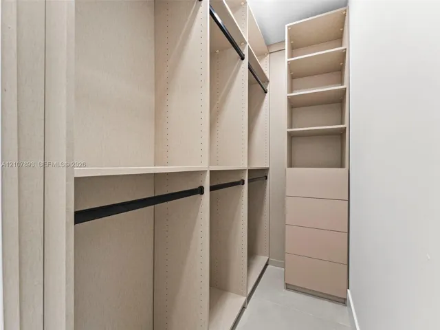 Custom reach-in closet featuring floor-to-ceiling shelving, integrated drawer stack, multiple hanging rods with matte black finish, and textured light-toned cabinetry