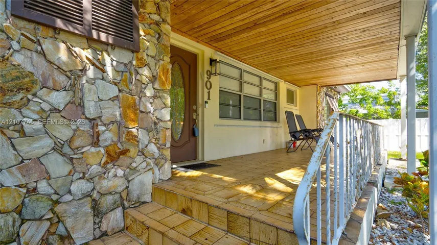 Covered porch featuring a wood-plank ceiling, natural stone facade, tiled flooring, and decorative metal railing