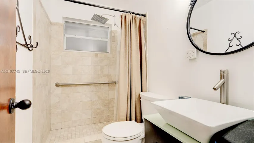 Bathroom featuring a vessel sink with a tall-profile faucet, vanity with a light-toned countertop, shower with stone-tile surround, and ceiling-mounted rainfall showerhead