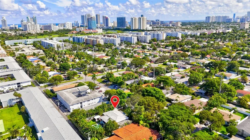 Aerial perspective of a residential property featuring a pitched roof, mature trees, and an urban cityscape horizon