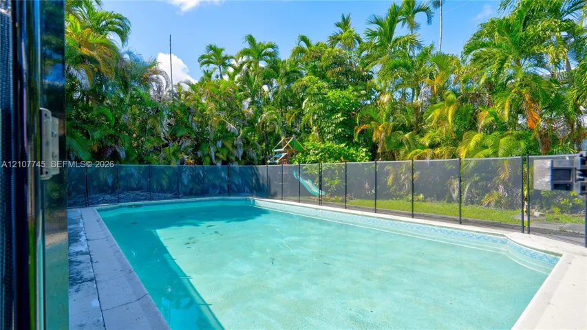 In-ground swimming pool featuring a perimeter safety fence, concrete pool deck, and mature palm tree landscaping