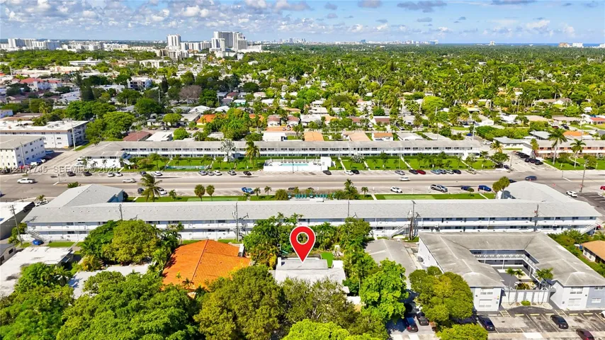 Aerial perspective of residential lot featuring mature trees, a multi-story building, and surface parking