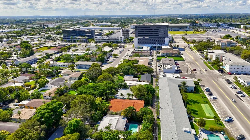 Aerial perspective of the property featuring a rectangular swimming pool, mature canopy trees, tiled roof structures, and paved road access
