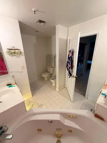 Bathroom featuring a white corner jetted soaking tub, tiled flooring, built-in vanity, toilet, and bidet