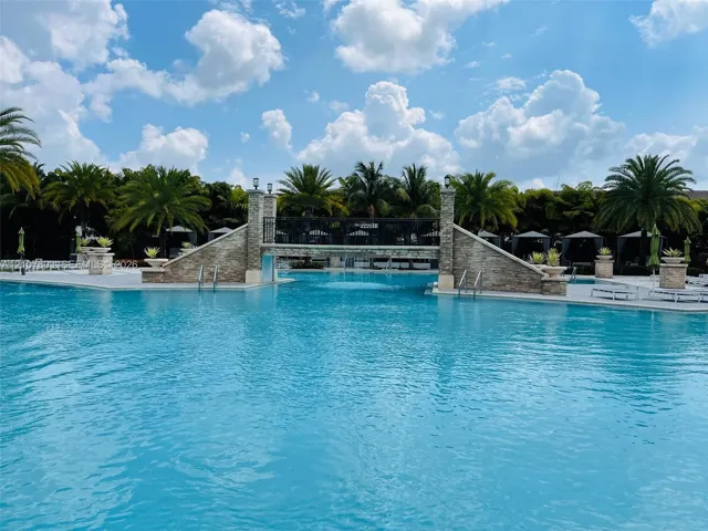 Swimming pool featuring a stone-clad pedestrian bridge, metal railings, integrated stone planters, and paved decking
