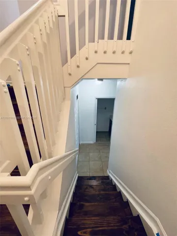 Staircase featuring stained wood treads, white-painted wood balusters, and a solid wood handrail with ceramic tile flooring at the base