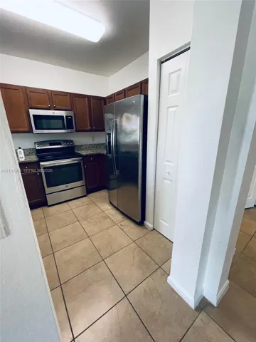 Kitchen featuring dark-toned cabinetry, stone-finish countertops, stainless steel appliances, ceramic tile flooring, and a floor-to-ceiling bi-fold door pantry