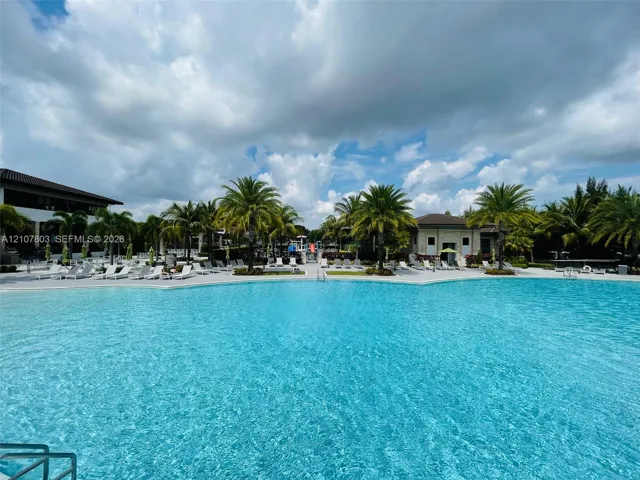 Large swimming pool featuring a zero-entry edge, expansive paved surround, and perimeter palm trees