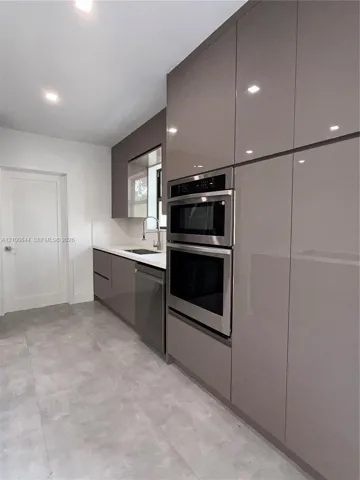High-gloss cabinetry, built-in stainless steel double wall ovens, integrated dishwasher, solid surface countertops, and large-format tile flooring