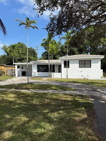 Single-story exterior featuring white stucco siding, a tiled roof, a covered carport, and mature palm landscaping