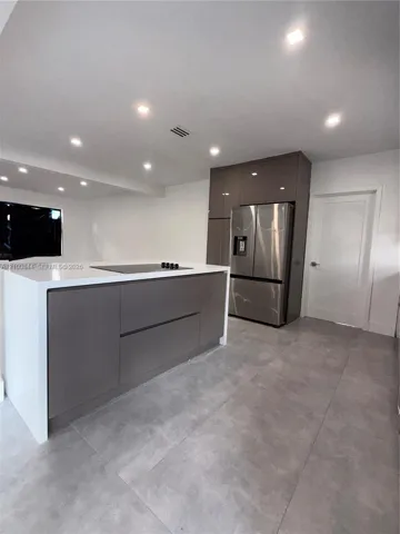 Modern kitchen featuring a central island with a waterfall countertop, high-gloss flat-panel cabinetry, stainless steel French-door refrigerator, and large-format tile flooring