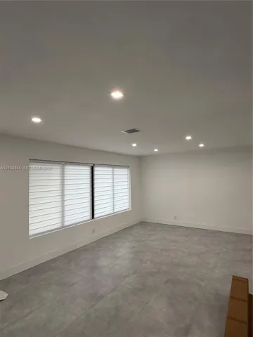 Neutral-toned interior space featuring light grey large-format tile flooring, recessed ceiling lighting, and expansive windows fitted with horizontal blinds