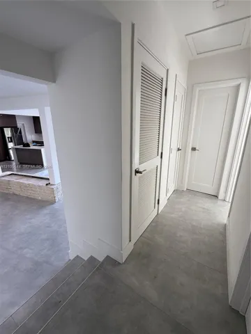 Hallway featuring large-format tile flooring, solid-core interior doors with satin nickel hardware, and a louvered utility closet​​‌​​​​‌​​‌‌​‌‌​​​‌‌​‌​‌​‌​​​‌​​ door