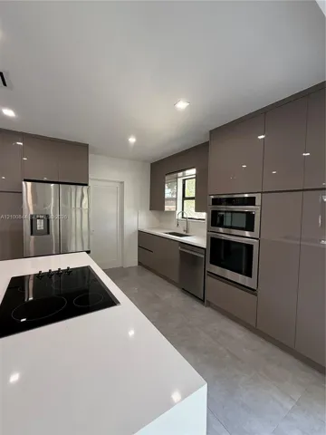 Kitchen featuring high-gloss cabinetry, a quartz countertop island with an integrated electric cooktop, stainless steel wall-mounted oven and microwave, and large-format tile flooring