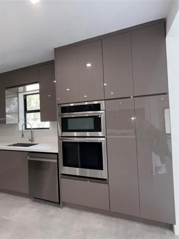 Kitchen featuring high-gloss cabinetry, stainless steel built-in double ovens, integrated dishwasher, solid surface countertops, and an undermount sink with a gooseneck faucet