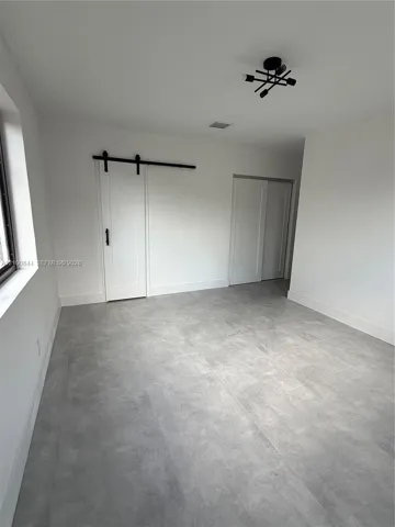 Room featuring grey stone-finish tile flooring, a white sliding barn door with matte black hardware, and a modern geometric flush-mount light fixture