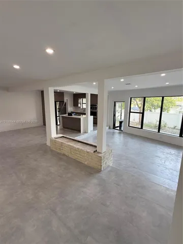 Large-format tile flooring, recessed lighting, brick-accented partition wall, kitchen island with stone-surface countertop, and expansive window wall with external door