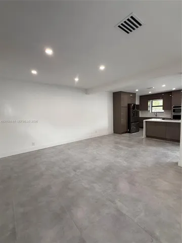 Large-format grey tile flooring, recessed ceiling lighting, glossy flat-panel cabinetry, and a kitchen island with stone-surface countertops