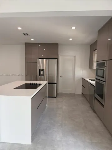 Kitchen featuring high-gloss cabinetry, stone-finish countertops, stainless steel appliances, a central island with a built-in cooktop, and large-format tile flooring