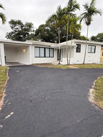 Single-story residence featuring white masonry exterior, attached carport, covered entryway, and mature palm trees