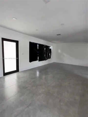 Open-concept interior featuring large-format tile flooring, neutral wall finishes, recessed ceiling lighting, and a multi-pane glass-panel exterior door