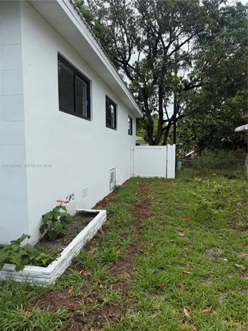 Stucco exterior featuring black-framed windows, a built-in raised brick planter, and a white vinyl privacy gate