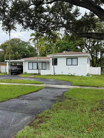 Single-story exterior featuring white masonry walls, a tile roof, an attached carport, and window frames with black trim