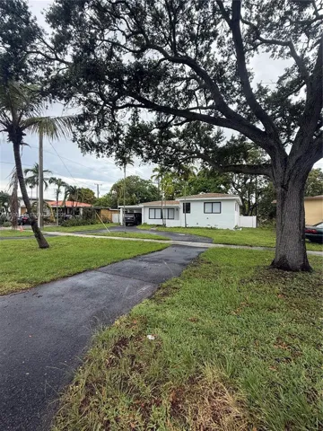 Single-story residence featuring a painted masonry exterior, covered carport, asphalt driveway, and mature landscaping