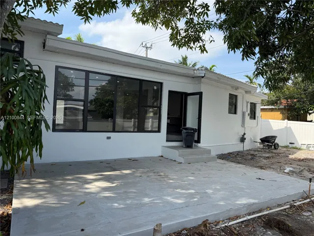 Concrete patio featuring large-format windows with dark frames, white exterior finish, and a single-step entry door