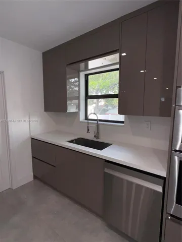 Modern kitchen featuring high-gloss cabinetry, stone-surface countertops, a stainless steel undermount sink, a gooseneck faucet, and integrated stainless steel appliances