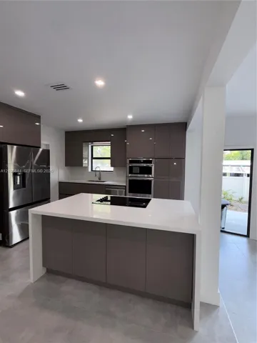 Modern kitchen featuring high-gloss cabinetry, a white waterfall-edge island, a recessed glass cooktop, stainless steel appliances, and large-format tile flooring