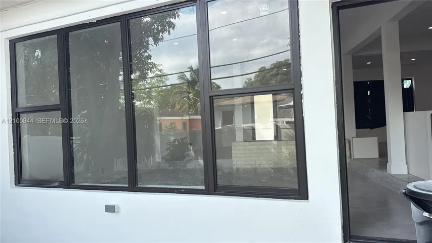 Large exterior window assembly featuring dark metal frames and horizontal sliding panels, paired with a matching dark-framed doorway and white exterior wall finish