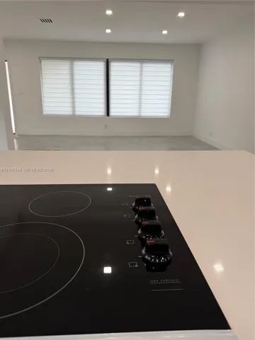 Black glass cooktop set into a white quartz countertop, complemented by recessed ceiling lighting and window blinds