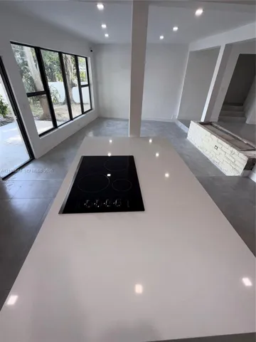 Kitchen island featuring a solid-surface countertop and a built-in electric cooktop, complemented by large-format tile flooring, recessed lighting, and expansive windows with black frames