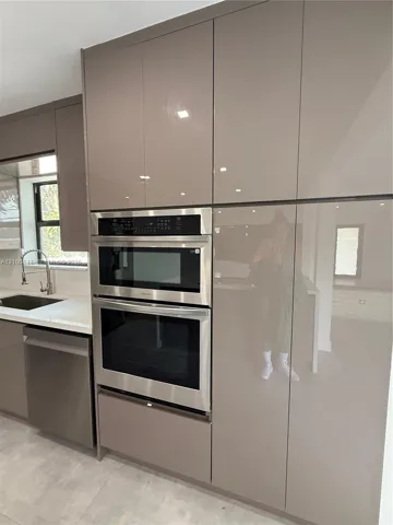 Modern kitchen featuring high-gloss cabinetry, integrated double wall ovens, a stainless steel dishwasher, and stone countertops with an undermount sink