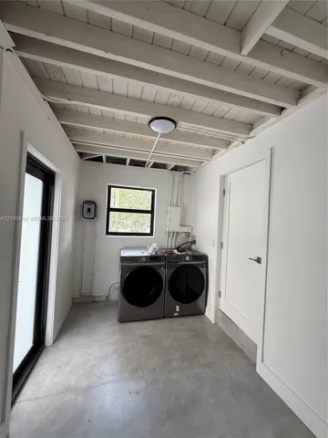 Utility space featuring exposed beam ceilings, concrete flooring, a single-pane window with black framing, and a full-light door with black framing