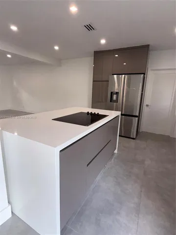 Kitchen island featuring a white stone countertop with an integrated electric cooktop and taupe cabinetry, stainless steel French-door refrigerator, and large-format tile flooring