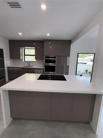 Kitchen featuring a central island with a waterfall countertop and integrated cooktop, flat-panel cabinetry, and stainless steel built-in double ovens