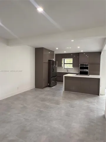 Kitchen featuring high-gloss slab cabinetry, central island with stone-surface countertop, built-in double wall oven, and large-format porcelain tile flooring