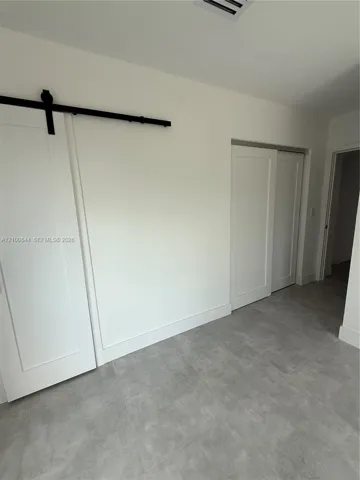 White sliding barn door with matte black hardware, grey tile flooring, and additional dual-panel sliding doors