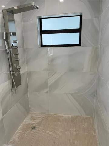 Walk-in shower featuring large-format porcelain tile, stainless steel rainfall shower panel with integrated handheld sprayer, and horizontal sliding window