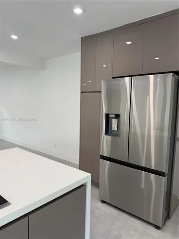 High-gloss cabinetry with floor-to-ceiling storage, stainless steel refrigerator with exterior water dispenser, island featuring a solid-surface countertop, and recessed ceiling lighting