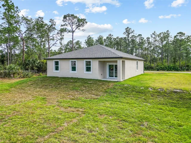 Rear elevation featuring a stucco exterior, hipped roof, sliding glass doors, and expansive grassy grounds surrounded by mature trees