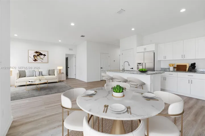 Open-concept living space featuring wood-finish flooring, recessed lighting, white cabinetry, a kitchen island with stone-finish countertops, and stainless-steel appliances