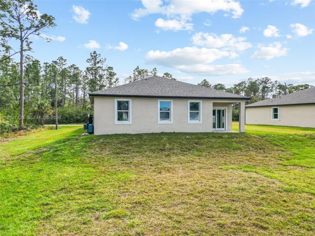 Stucco exterior, hipped roof, glass sliding door, and expansive rear lawn