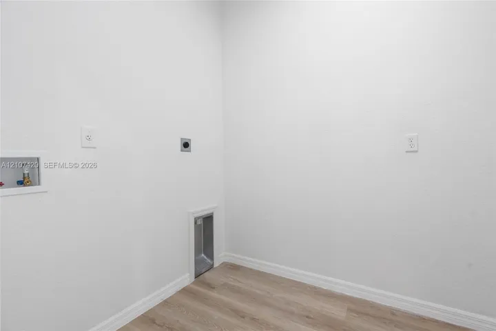 Utility area featuring wood-finish flooring, recessed water supply and drainage hookups, and a dedicated wall-mounted dryer vent