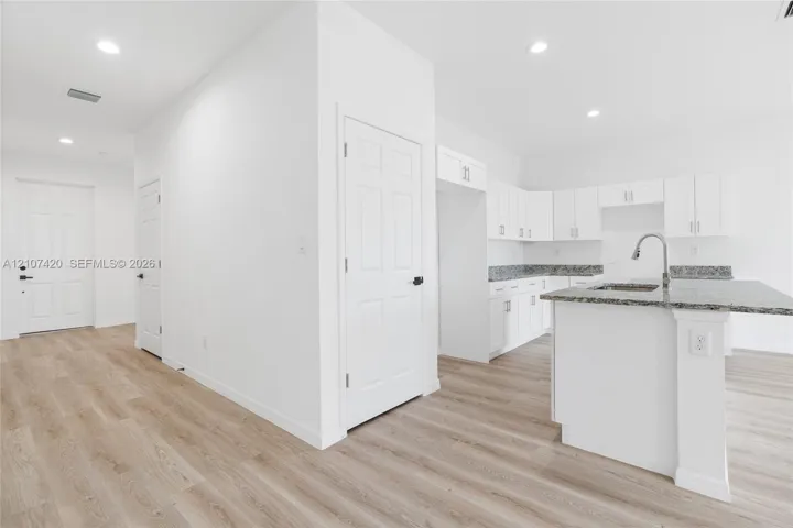 Kitchen featuring white cabinetry, stone-finish countertops, an integrated island, a stainless steel faucet, and wood-finish flooring
