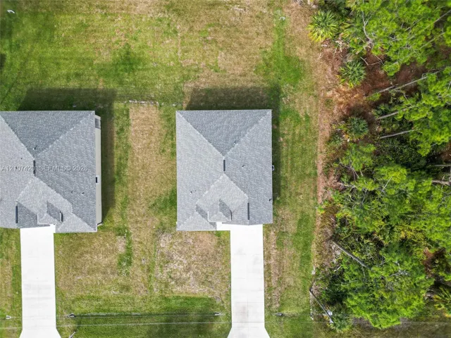 Aerial perspective featuring expansive grass lots, asphalt shingle rooflines, concrete driveways, and mature pine tree borders